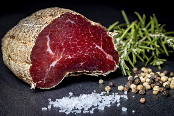 Delicious sausage with salt and pepper on a dark slate plate, delicacy ham fresh from the butcher