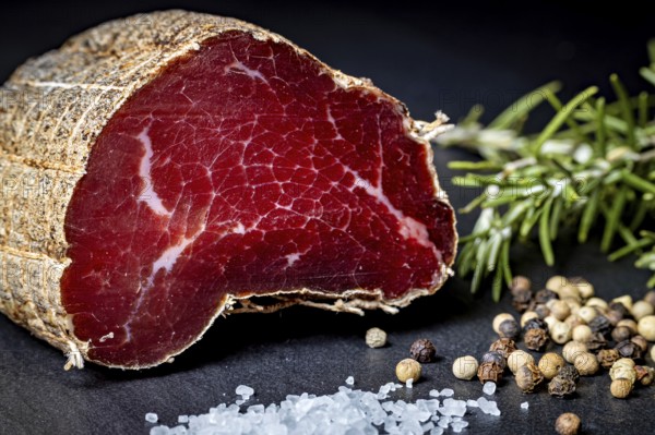 Juicy piece of sausage on a dark background with herbs and spices, delicacy ham fresh from the butcher