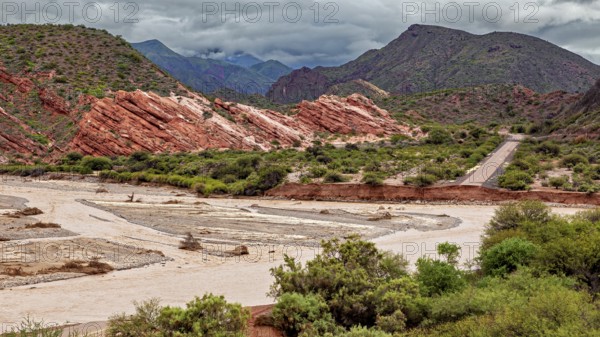 Picturesque valley with road surrounded by red rocks and green vegetation, the landscape and colorful rock formations of the Quebrada de Cafayate near Salta in Argentina