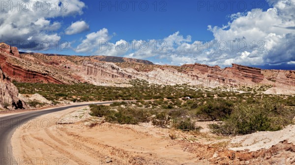 Road snakes through red rocky landscape under a cloudy sky, the landscape and colorful rock formations of Quebrada de Cafayate near Salta in Argentina