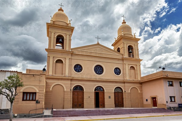 Front view of a church with two bell towers, in front of an empty forecourt under partly cloudy sky, the Catedral de Nuestra Señora del Rosario in Cafayate, Argentina