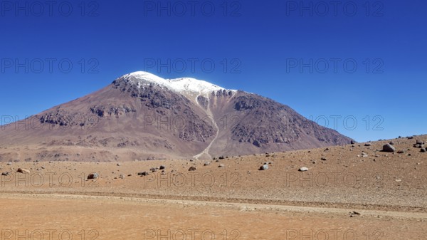 A bizarre mountain with a snow-capped summit rises above the dry desert, the landscape and colorful rock formations of the Quebrada de Cafayate near Salta in Argentina