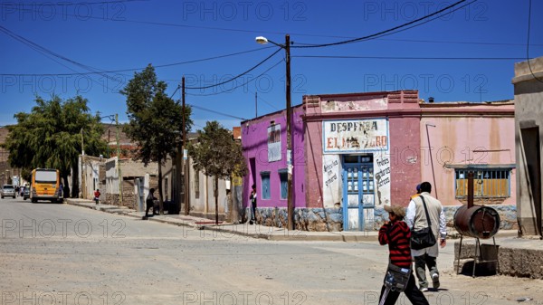 Colourful buildings and people in a bright, dry village with hills in the background, San Antonio de los Cobres, Salta Province, Argentina