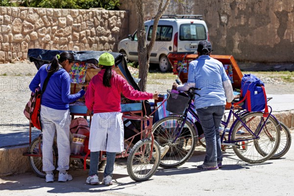 Three woman standing at roadside carts with bicycles, people in the streets of San Antonio de los Cobres, Salta province, Argentina