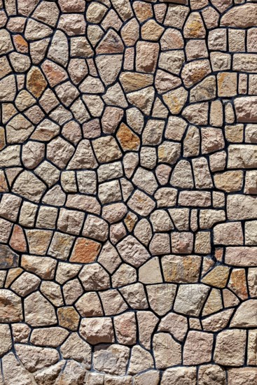 Irregular natural stone wall with brown-beige stones in rustic pattern, a natural stone wall as a background
