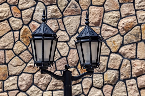 Two vintage style black lanterns in front of a stone wall, two old street lamps in front of a natural stone wall as a backdrop