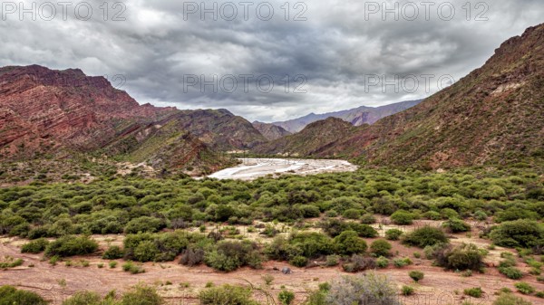 A green valley surrounded by mountains under a cloudy sky, the landscape and colorful rock formations of the Quebrada de Cafayate near Salta in Argentina