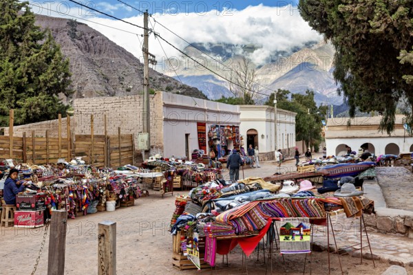 A marketplace with colorful fabrics and stalls in front of a majestic mountain landscape, tourist and souvenir market of Santa Rosa de Tastil near Salta in Argentina