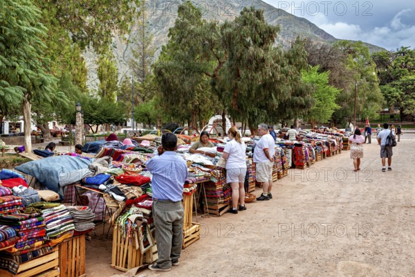 People check out textile stalls at a lively market against a mountain backdrop, tourist and souvenir market of Santa Rosa de Tastil near Salta in Argentina