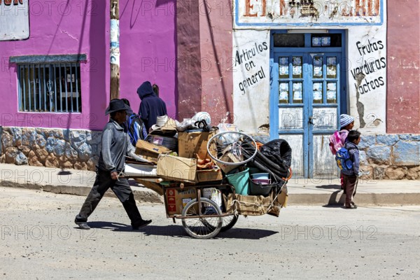 Man pulls a cart full of boxes along a colorful street, people in the streets of San Antonio de los Cobres, Salta province, Argentina