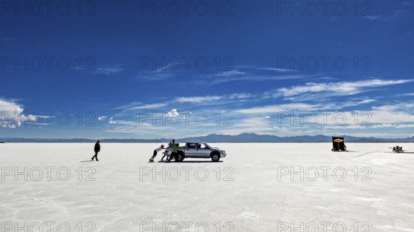 People push a car on a wide salt lake under a blue sky, The Salar de Cauchari salt pan near Salta in Argentina