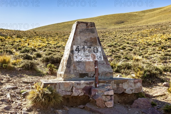 Stone pyramid with altitude marker at 4130 meters, surrounded by dry desert landscape under blue sky, monument on the Cuesta de Lipán pass in the province of Jujuy in northern Argentina