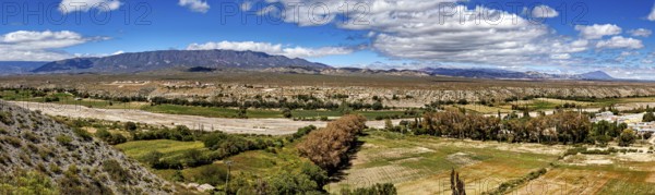 Panoramic view of green valleys and distant mountains under a cloudy sky, roads through the Quebrada de Cafayate countryside near Salta in Argentina
