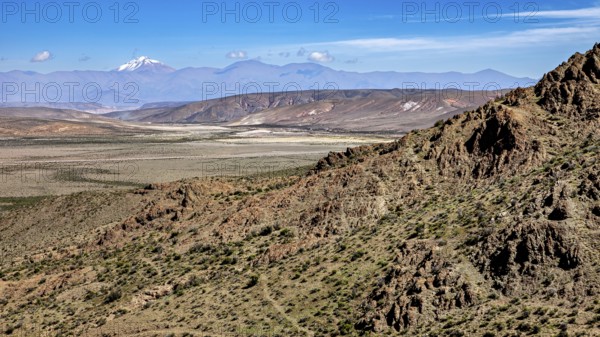 Vast desert with rocky mountain range and blue sky in the background, roads through the Quebrada de Cafayate countryside near Salta in Argentina