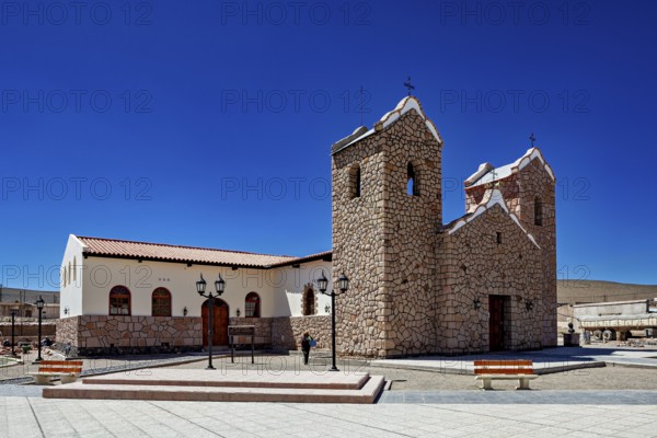 Stone church with two towers under clear blue sky in an open square with lanterns, Parroquia San Antonio de Padua in San Antonio de los Cobres
