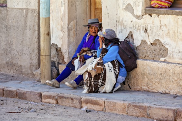Two woman in traditional clothes talking on a wall, people in the streets of San Antonio de los Cobres, Salta province, Argentina