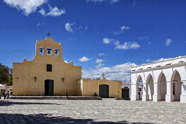 Yellow church with bell tower in front of a large square under bright blue sky, Iglesia San José de Cachi in Argentina