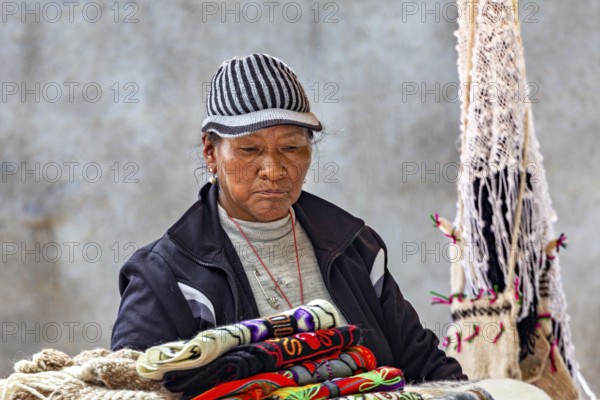A woman in traditional clothing looks at handmade textiles with serious expression, tourist and souvenir market of Santa Rosa de Tastil near Salta in Argentina