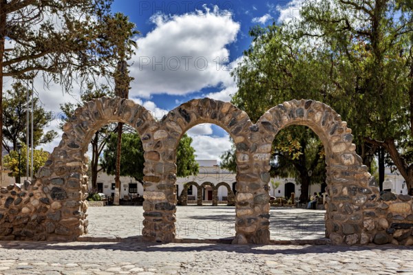 Stone arches on a sunny square with trees and partly cloudy sky, Downtown Cachi in Argentina
