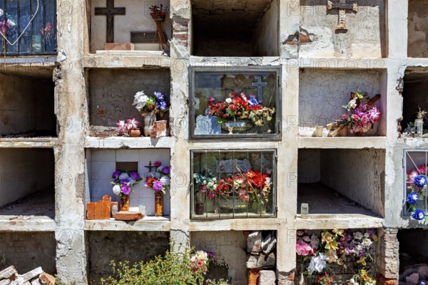 Tomb niches in a weathered wall decorated with flowers and crosses, The Cachi cemetery in Argentina