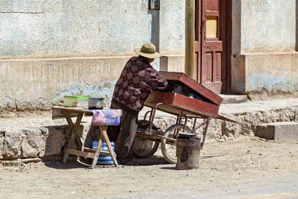 Man working on a red-roofed cart on the street corner, people in the streets of San Antonio de los Cobres, Salta province, Argentina