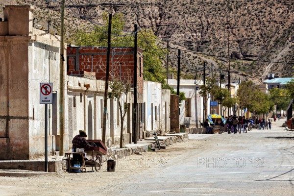 People walk along a picturesque rural road with old buildings and trees, San Antonio de los Cobres, Salta Province, Argentina
