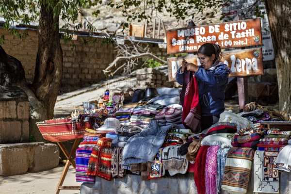 A market stand with colorful blankets and textiles in a sunny village environment in the Andes, tourist and souvenir market of Santa Rosa de Tastil near Salta in Argentina