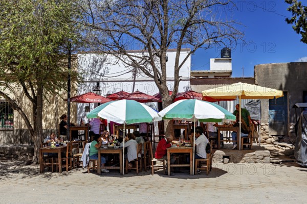 Outdoor area with dining tables and colorful umbrellas where people sit in the shade in sunny weather, Downtown Cachi in Argentina
