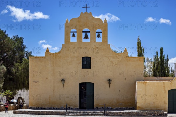 Front view of a yellow church with bells and cross under a blue sky, Iglesia San José de Cachi in Argentina