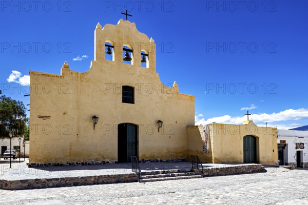 Yellow church with bell tower and cross against a clear sky, colonial style of architecture, Iglesia San José de Cachi in Argentina