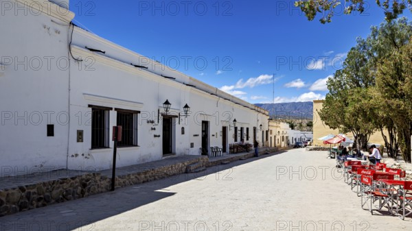 Wide street with white buildings and a patio with red chairs under a clear blue sky, Downtown Cachi in Argentina