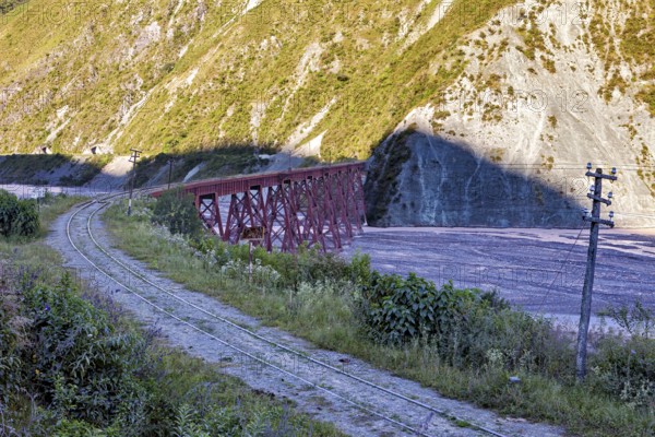 Abandoned railway line with red bridge in a mountainous landscape with lots of vegetation, roads through the Quebrada de Cafayate countryside near Salta in Argentina