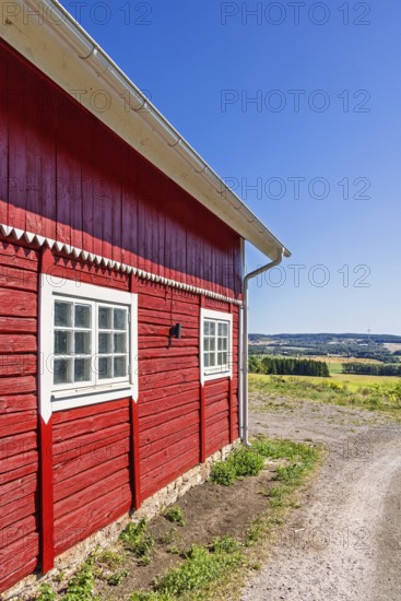 Red wooden rural barn beside a gravel road with a scenic landscape view in the countryside a sunny summer day, Sweden