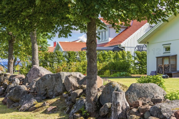 Peaceful residential scene featuring wooden houses with by large rocks and tree trunks in the garden at a suburban neighborhood, Sweden