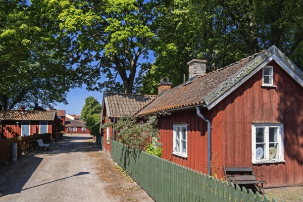 Peaceful Scandinavian street lined with traditional red wooden houses with green picket fence and lush green trees create a charming small town atmosphere in a classic swedish village, Lidköping, Sweden
