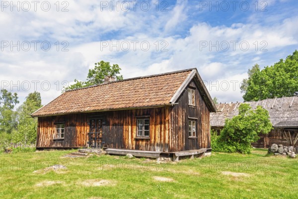 Old rustic wooden croft with weathered timber accompanied by a barn in a rural setting in a historic nordic craftsmanship and tradition countryside architecture a sunny summer day, Vara, Sweden