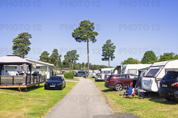 Family friendly campground featuring several caravans, parked cars along a paved pathway in a relaxed holiday atmosphere a sunny summer day with a clear blue sky, Lidköping, Sweden