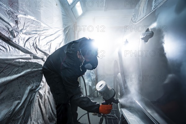 Auto body painter wearing a respirator mask and protective suit, carefully applying a fresh coat of paint to a vehicle door in a professional car repair and service workshop
