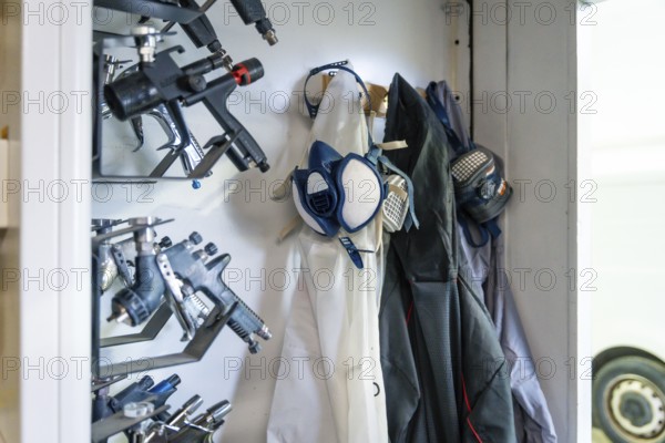 Organized racks of professional spray guns, respirators and protective suits in an automotive paint shop, highlighting safety, precision and clean workshop preparation