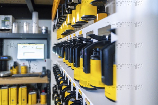 Automotive paint system with rows of yellow and black containers holding varied tints on organized shelves in a professional auto body shop for precise color matching and refinishing
