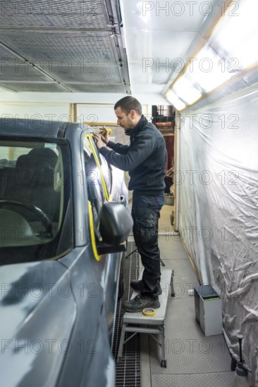 Mechanic applying masking tape meticulously on a car body before painting in a professional automotive repair and service workshop, ensuring precise preparation for a flawless finish