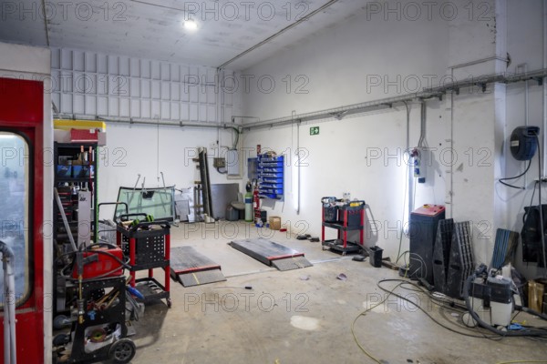 Empty car body shop interior with lifts, paint booth, tools and spare parts on carts and cabinets, bright, clean industrial garage ready for vehicle repair and painting