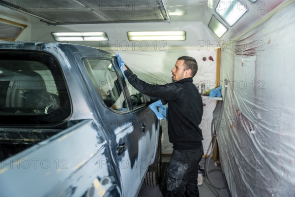 Auto body technician carefully cleaning and preparing a pickup truck in a professional paint booth, ensuring a smooth surface before applying new paint