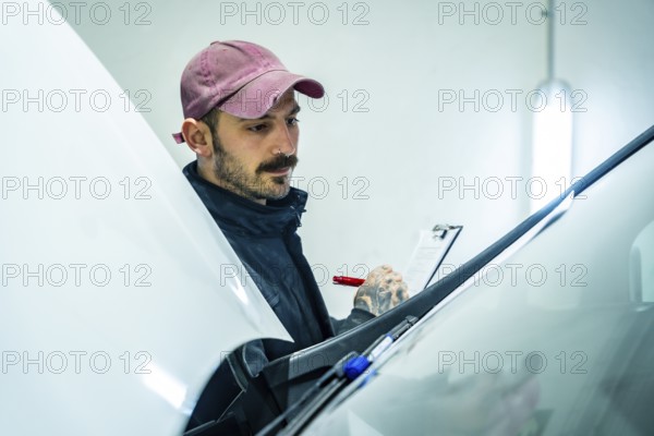 Auto repair shop worker checking a new vehicle, performing a meticulous inspection of the car body condition and noting down observations on a checklist