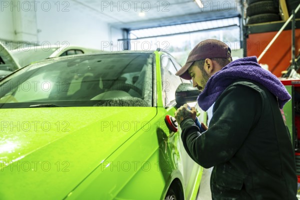 Auto body technician working on a vibrant green car, using a polisher to refine and enhance the fresh paint finish in a professional garage workshop during a vehicle detailing service