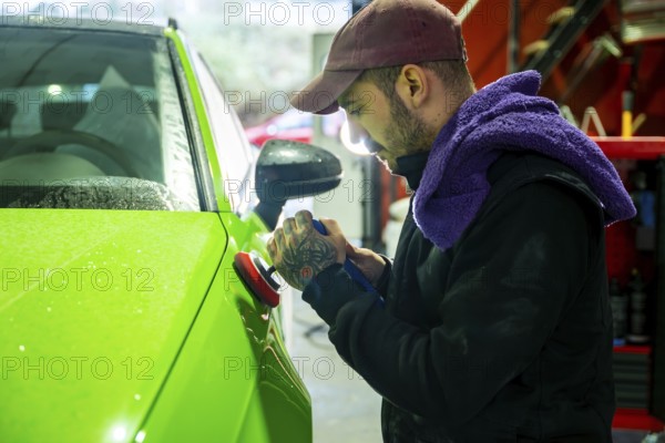 Mechanic meticulously polishing a vibrant green car body with a rotary polisher, improving its finish and removing imperfections during a detailing service in an automotive repair shop