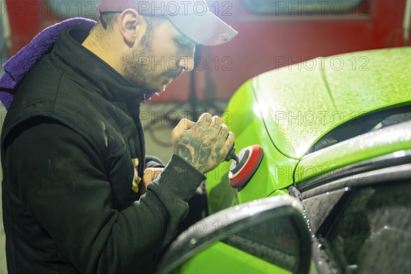 Automotive technician buffs vibrant green car paint with a professional orbital polisher in a garage, focusing on precision and shine during final detailing stages