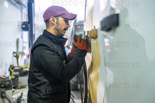 Auto body technician sanding a car panel in a repair shop, preparing the surface for painting during restoration work and maintaining vehicles in a professional workshop environment