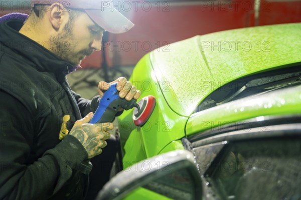Professional automotive technician using an orbital buffer to polish a glossy green car body in a detailing studio, demonstrating precision paint correction and vehicle care