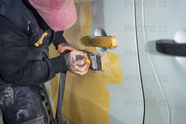 Auto body technician sanding a car door to prepare its surface for painting after repairs, demonstrating the meticulous process of vehicle restoration in an automotive workshop